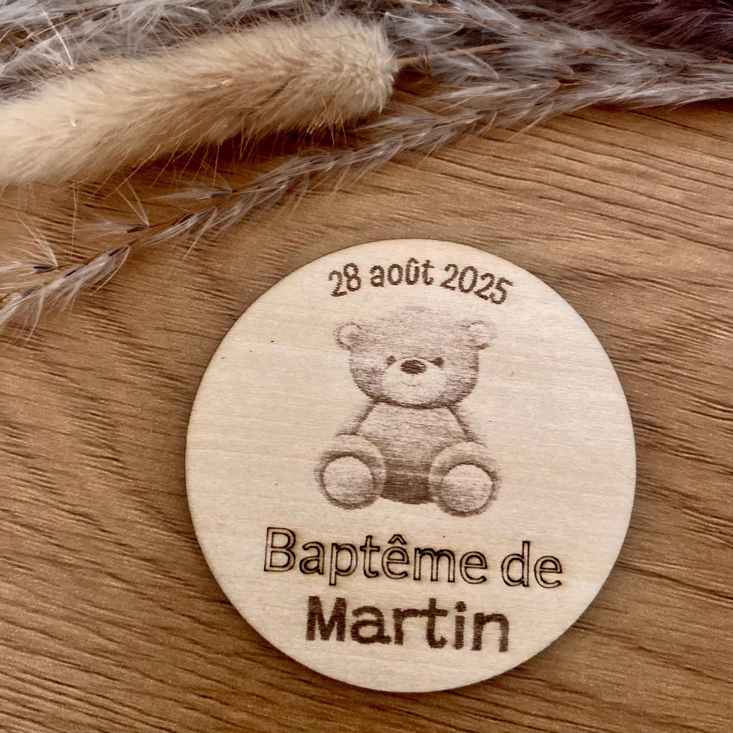 Magnet rond en bois personnalisé pour événement, gravé avec des motifs floraux et une date, présenté sur un fond épuré, parfait comme souvenir de baptême original."