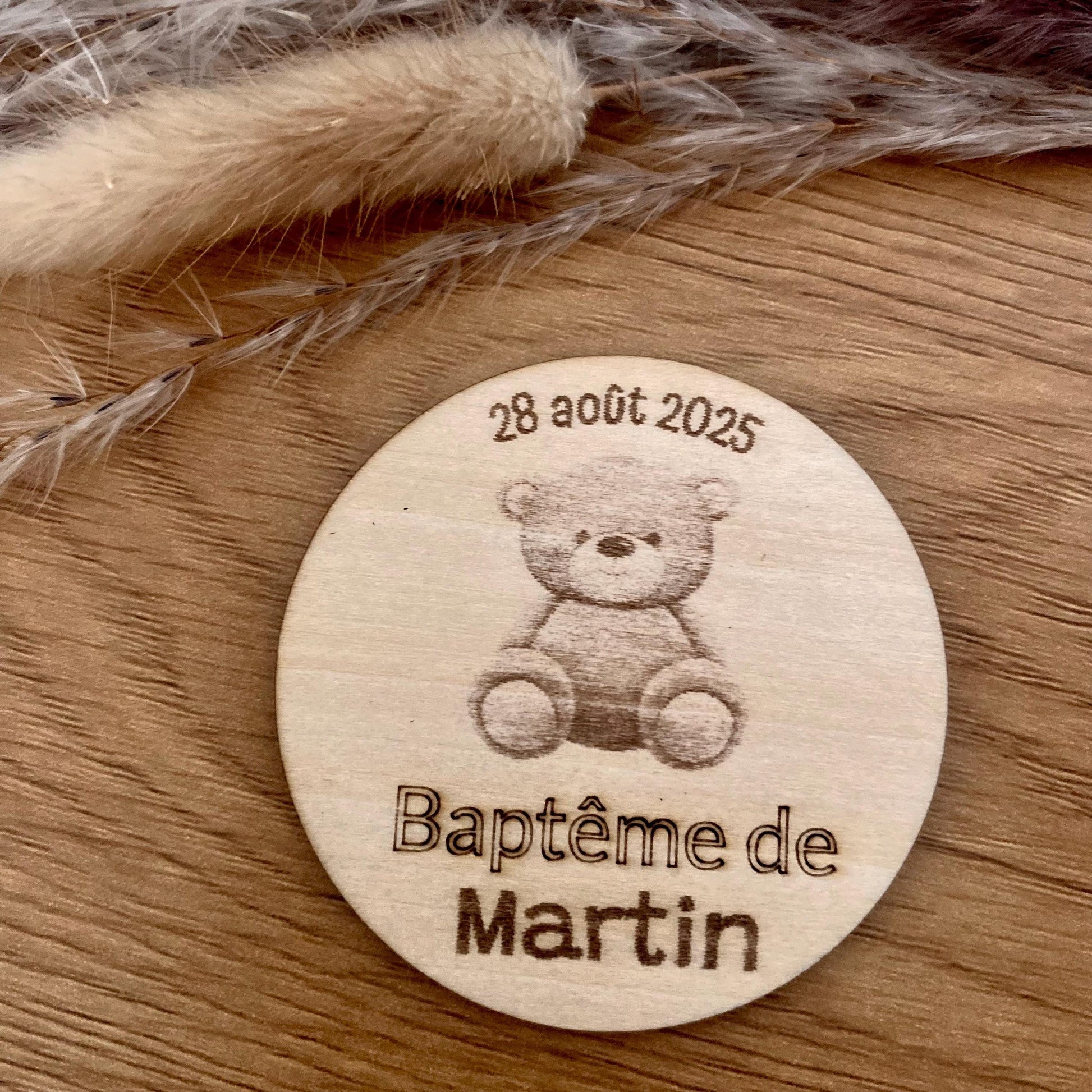 Magnet rond en bois personnalisé pour événement, gravé avec des motifs floraux et une date, présenté sur un fond épuré, parfait comme souvenir de baptême original."