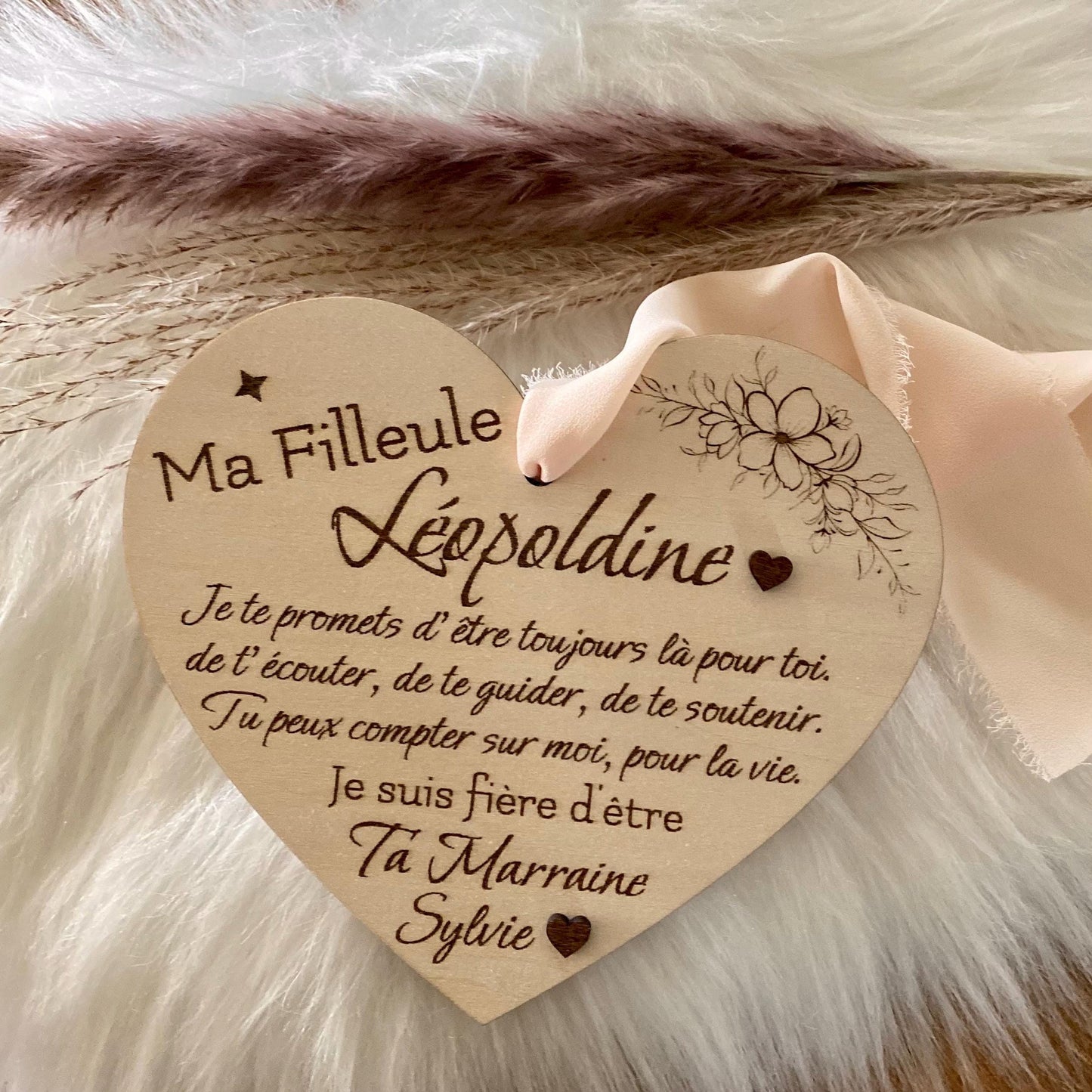 Carte cœur en bois avec ses détails floraux et les deux cœurs en relief, suspendue avec son ruban en mousseline beige.