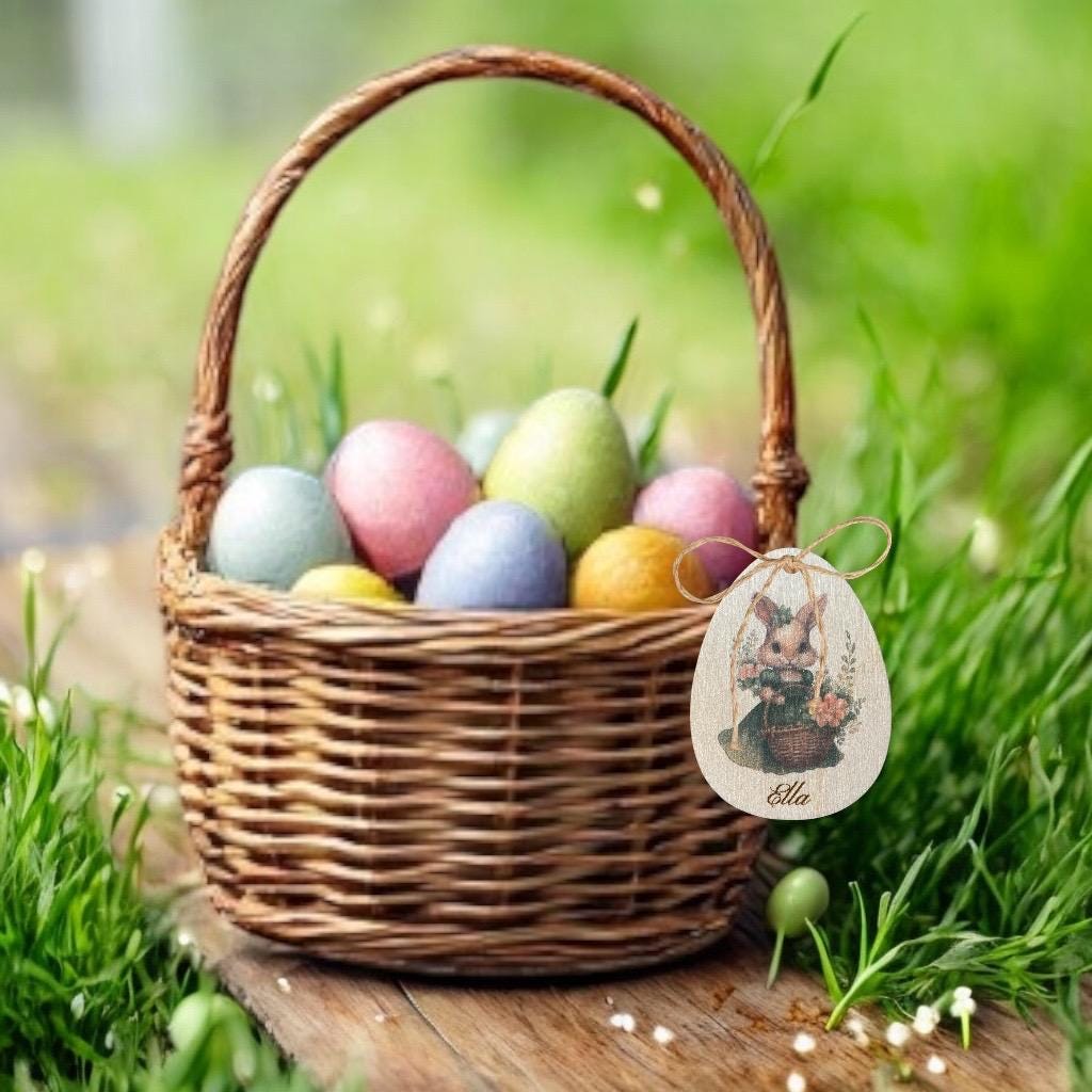 Étiquette en bois en forme d'œuf personnalisée avec un prénom, attachée à un panier en osier rempli d'œufs en chocolat.