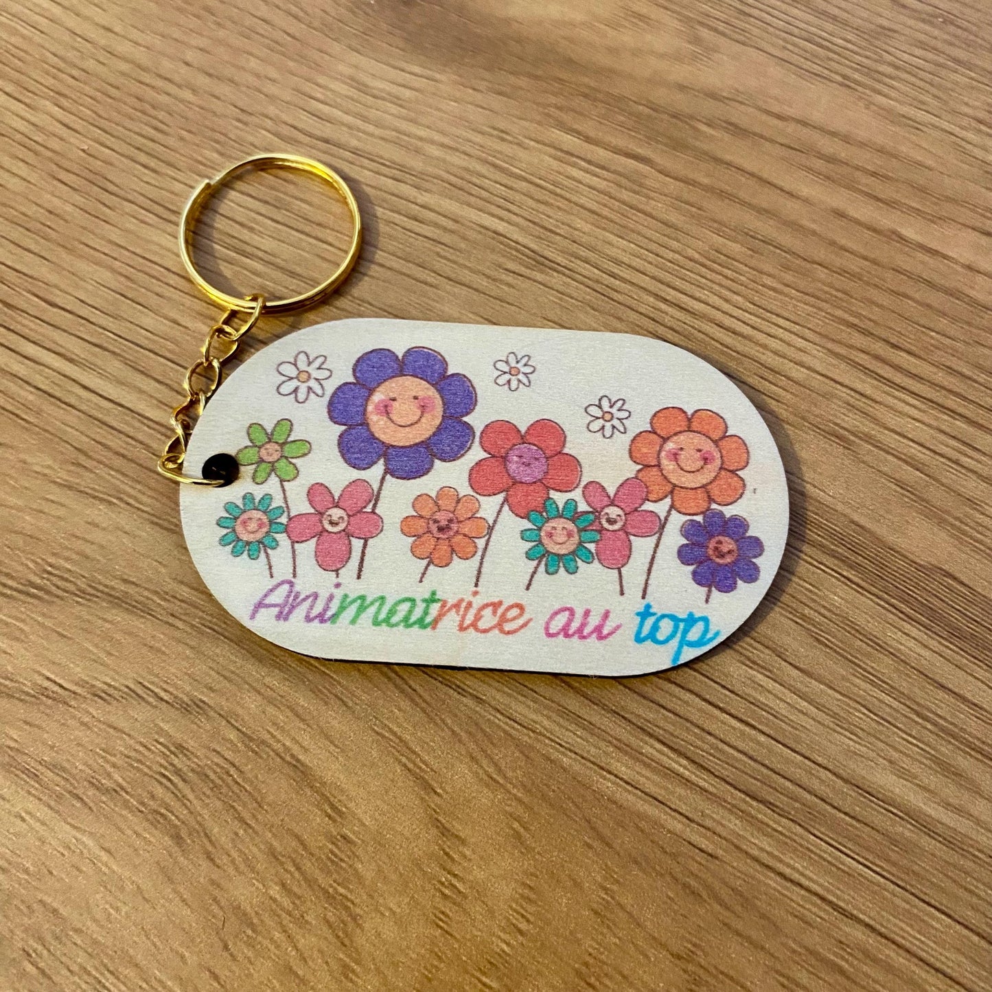 Magnet en bois et porte-clés assorti avec dessin floral d'enfant, présentés dans un emballage cadeau en papier de soie beige et raphia."