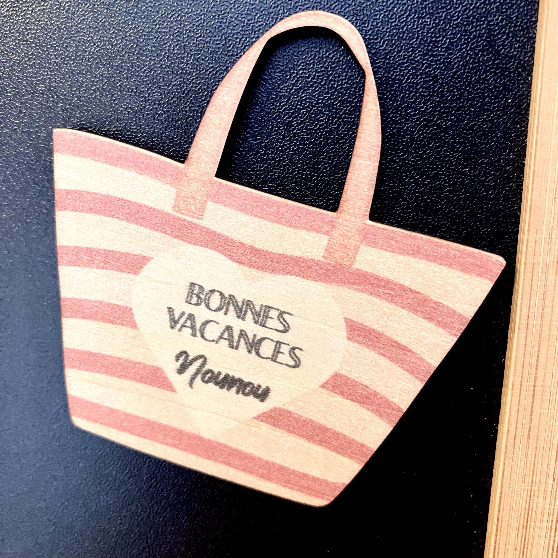 magnet, posé sur un support en bois, évoquant une ambiance de vacances."