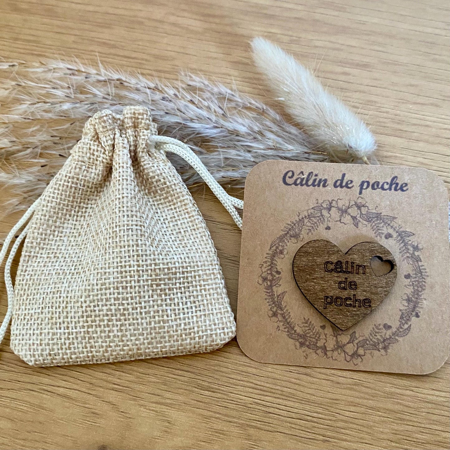 Câlin de poche coeur en bois gravé sur son support kraft et accompagné de son petit pochon