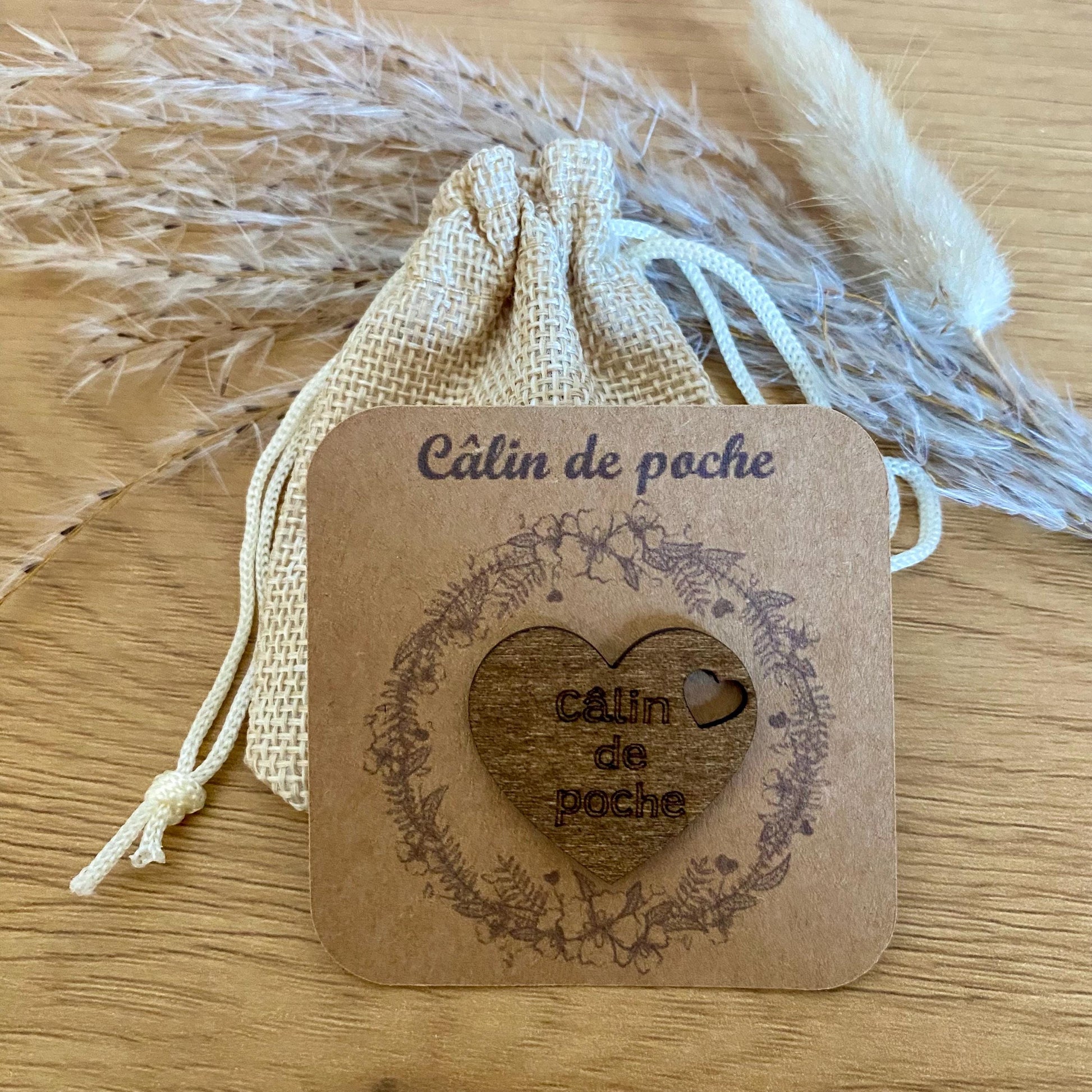 Câlin de poche coeur en bois gravé sur son support kraft et accompagné de son petit pochon