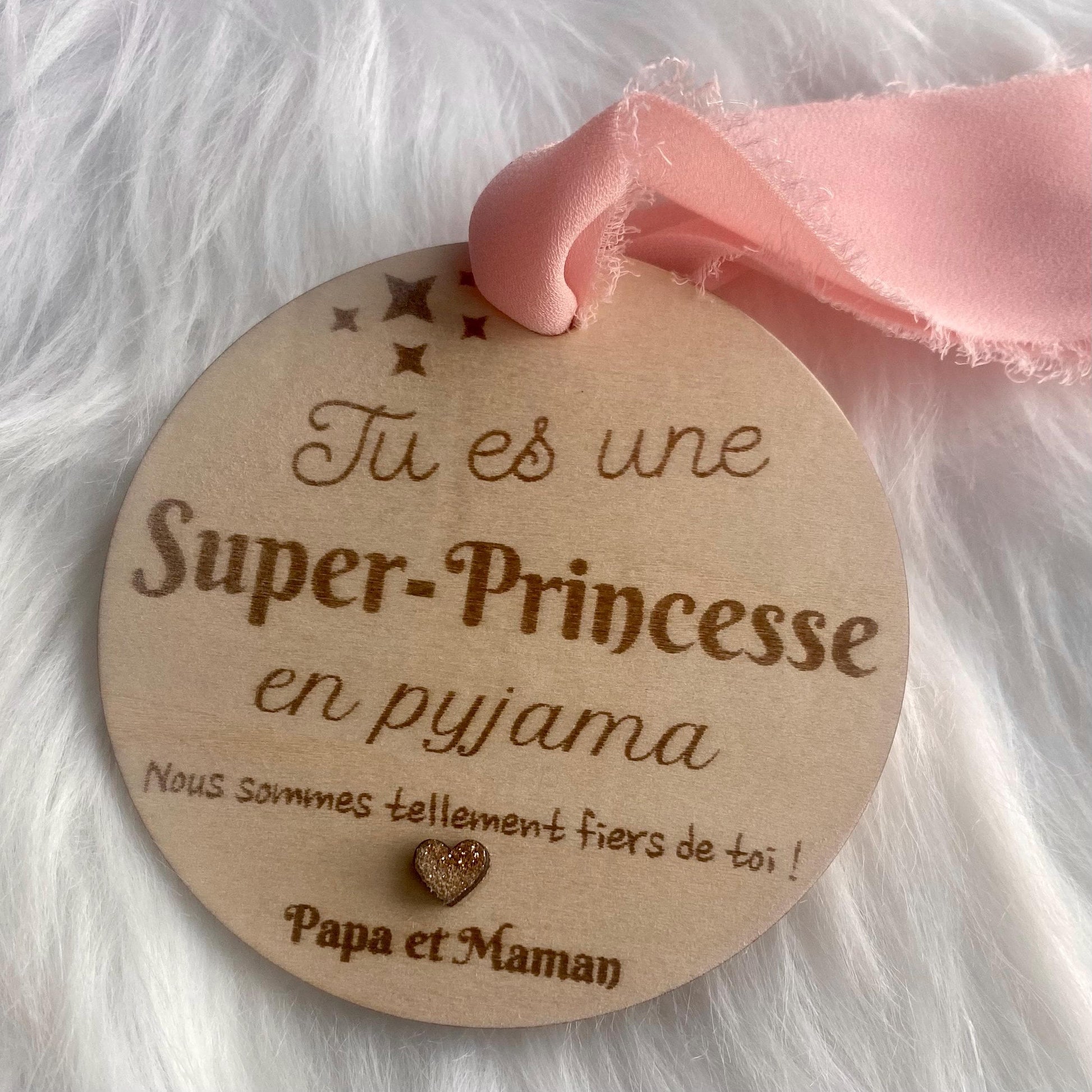 La suspension bois "Super-princesse" mise en valeur par un ruban coloré, avec une lumière douce et bienveillante.