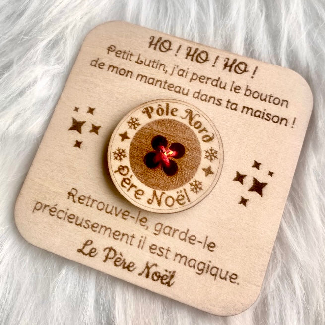 Une carte de Noël carrée en bois, La carte est gravée d'un message du Père Noël et comporte en son centre un bouton en bois véritable avec l'inscription "Pôle Nord" et "Père Noël" et un centre rouge brillant. La carte est entourée de petites étoiles gravées.
