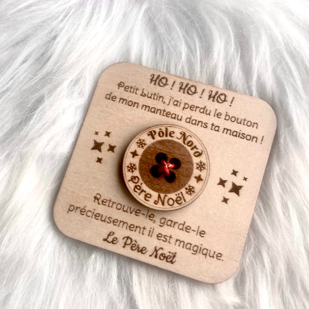 Une carte de Noël carrée en bois, La carte est gravée d'un message du Père Noël et comporte en son centre un bouton en bois véritable avec l'inscription "Pôle Nord" et "Père Noël" et un centre rouge brillant. La carte est entourée de petites étoiles