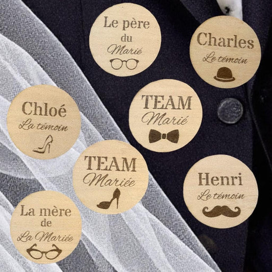 Sélection de badges de mariage en bois avec différents motifs (chapeau, talon) disposés sur un support élégant."