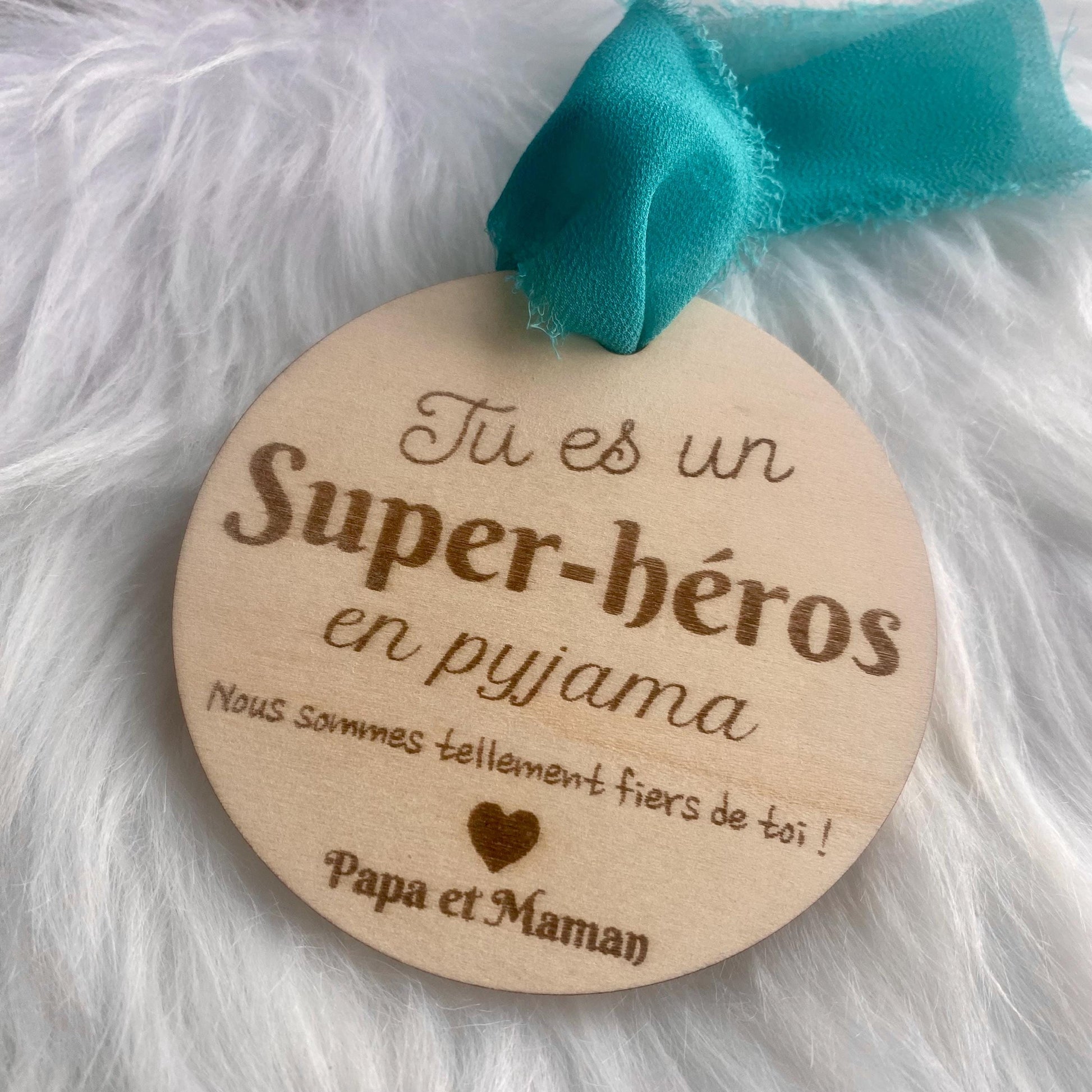 La suspension bois "Super-Héros" mise en valeur par un ruban coloré, avec une lumière douce et bienveillante.