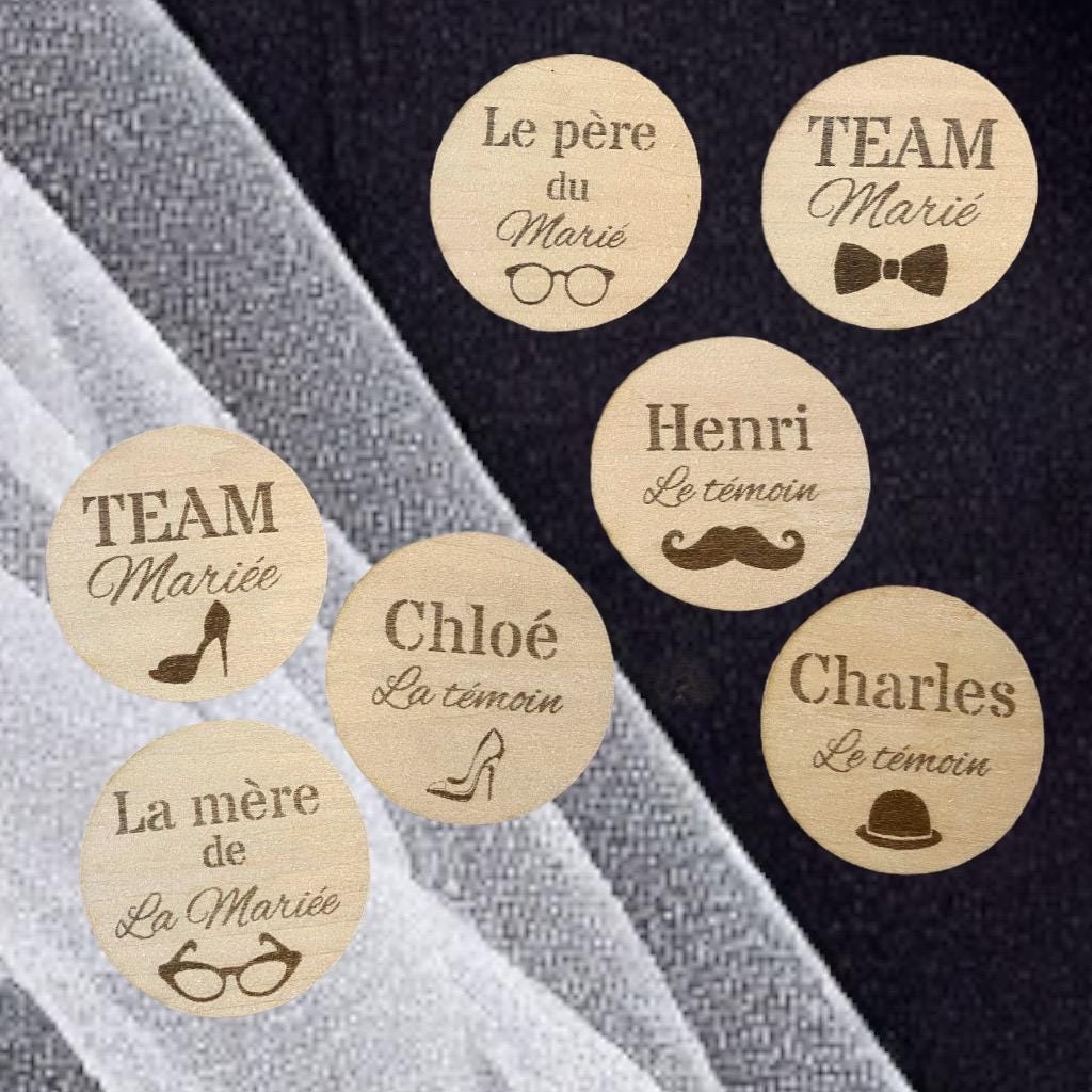 Sélection de badges de mariage en bois avec différents motifs (chapeau, talon) disposés sur un support élégant."