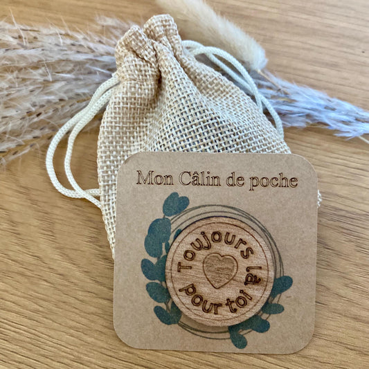"Jeton rond 'Petit Câlin' en bois présenté sur son support kraft, à côté de son petit pochon."