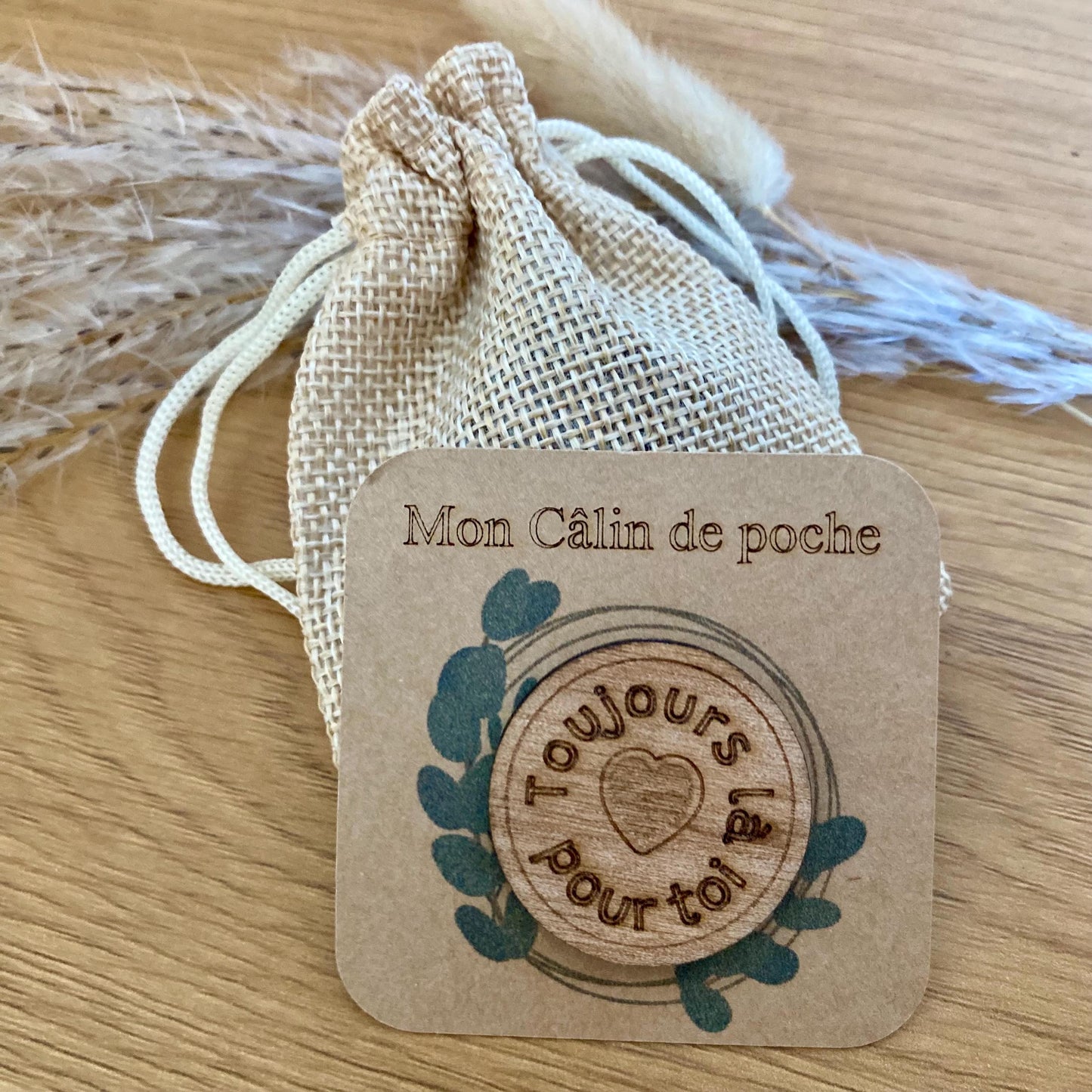 "Jeton rond 'Petit Câlin' en bois présenté sur son support kraft, à côté de son petit pochon."