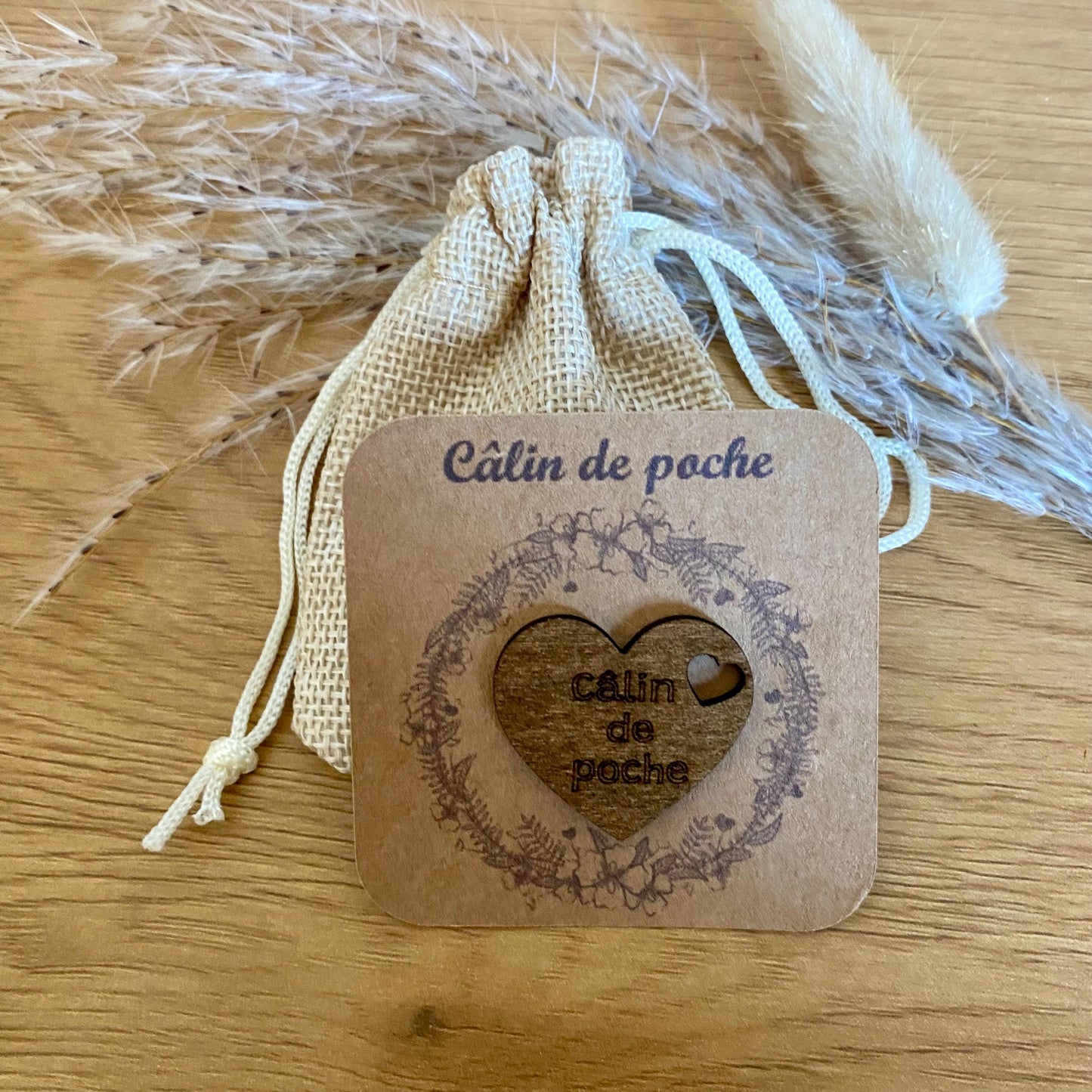 Câlin de poche coeur en bois gravé sur son support kraft et accompagné de son petit pochon