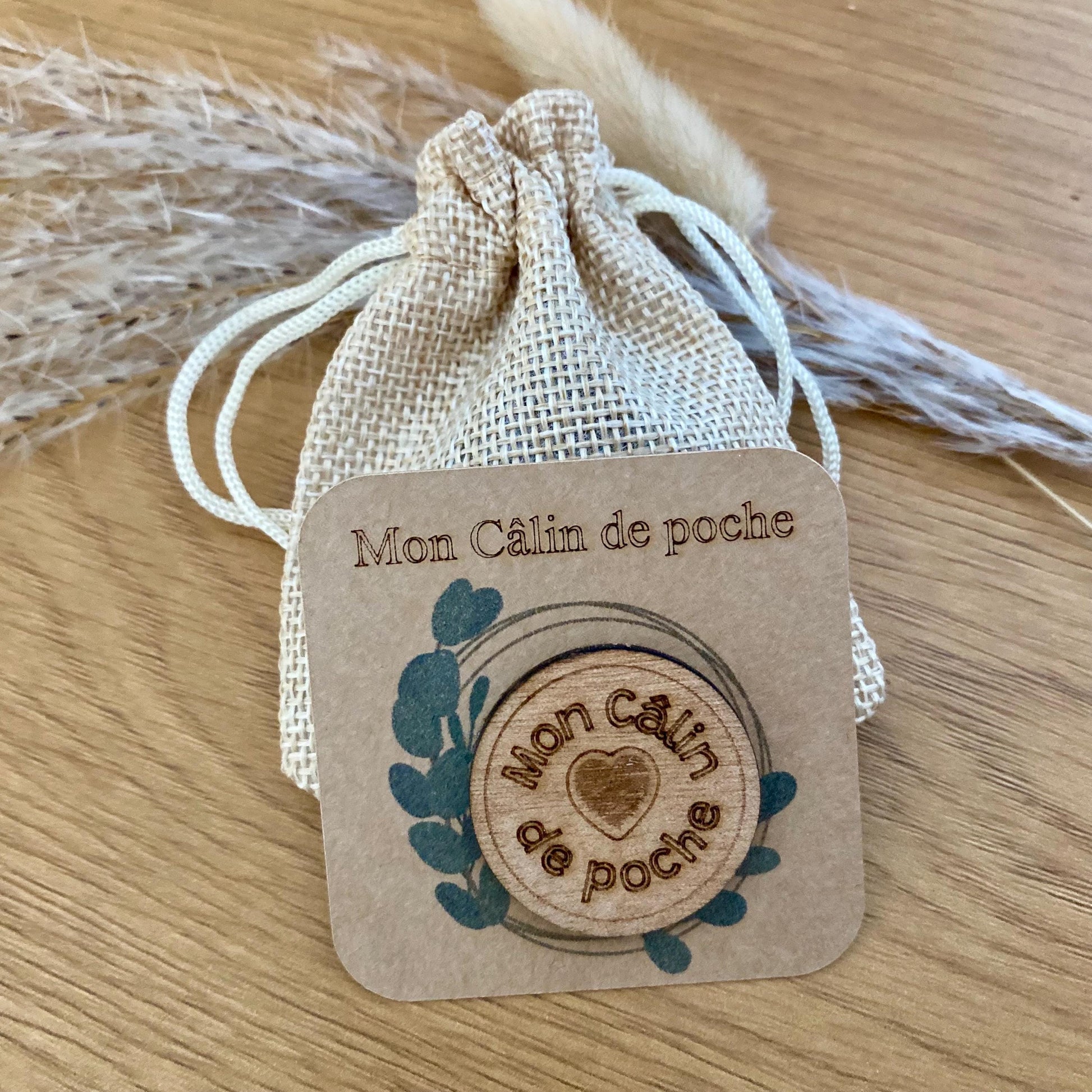 Jeton en bois 'Câlin de poche' posé sur son support en kraft, avec le pochon en tissu à côté.