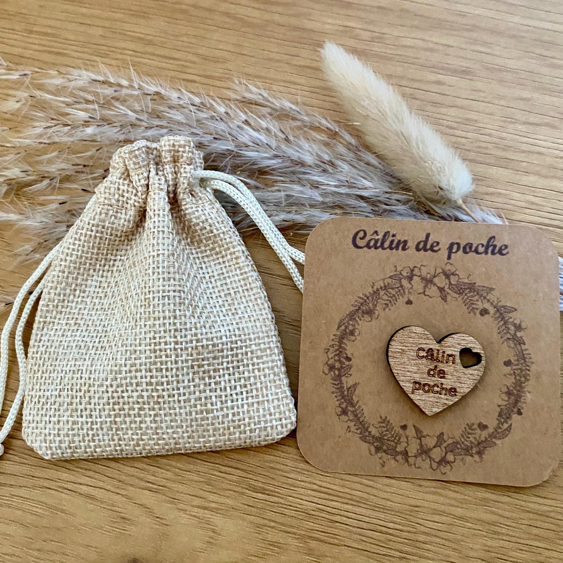 Un Câlin de poche en bois sur son petit support kraft présenté  à côté de son petit pochon .