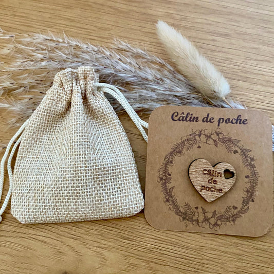 Un Câlin de poche en bois sur son petit support kraft présenté  à côté de son petit pochon .