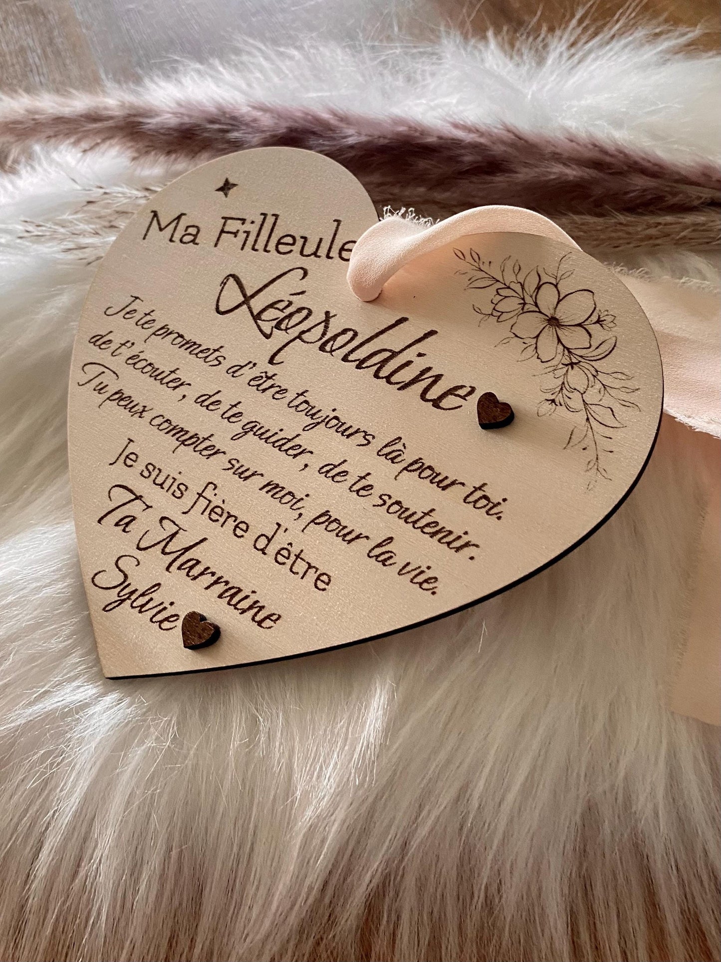Carte cœur en bois avec ses détails floraux et les deux cœurs en relief, suspendue avec son ruban en mousseline beige.
