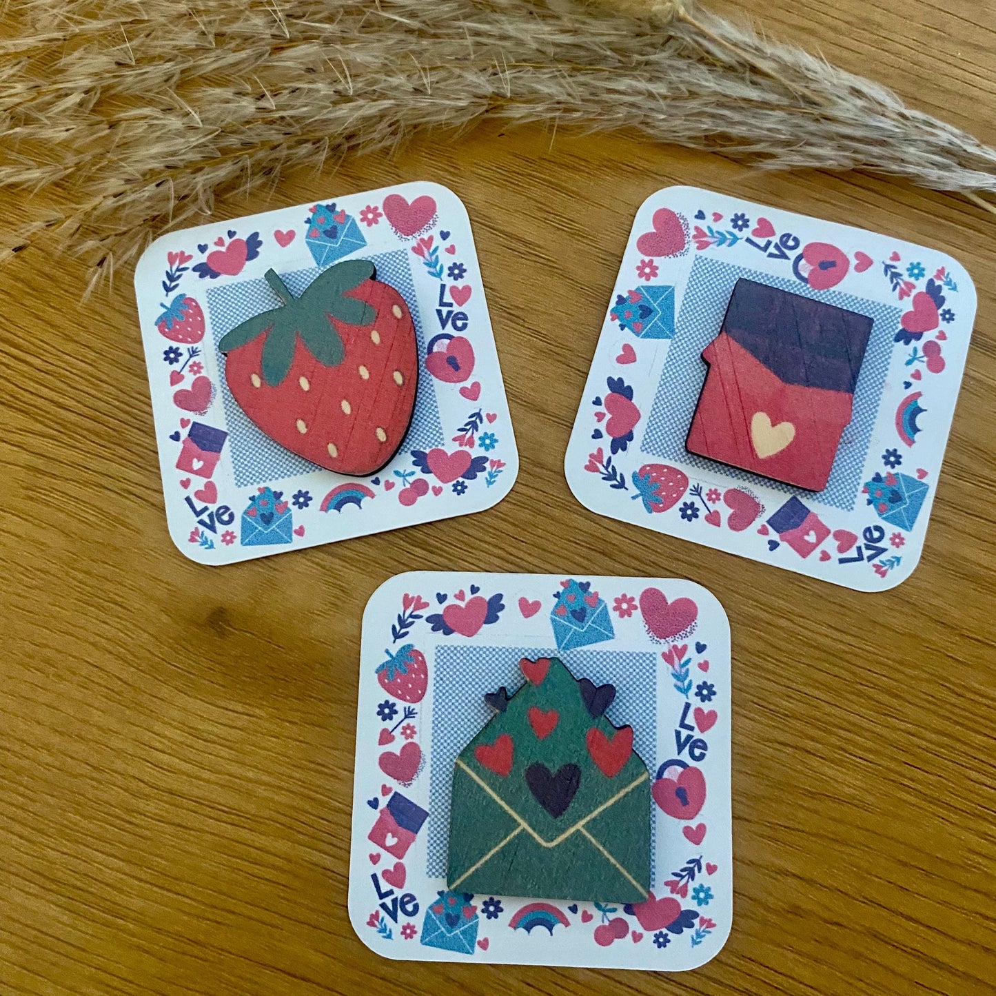 Les trois modèles de Câlins de Poche (enveloppe, fraise, tablette) présentés côte à côte, entourés de rubans en raphia.