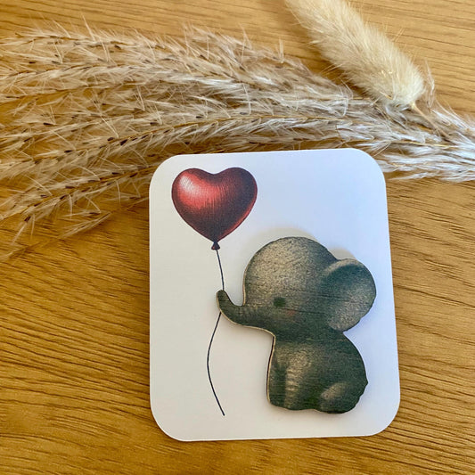 Petit éléphant en bois imprimé accompagné de sa carte de présentation, posé sur une surface naturelle."