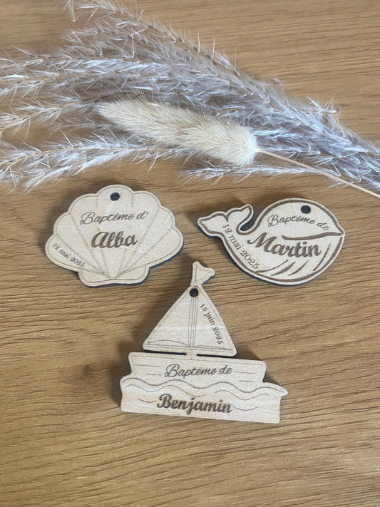 Sélection d'étiquettes en bois aux formes variées coquillage, baleine, bateau) posées sur un support neutre."