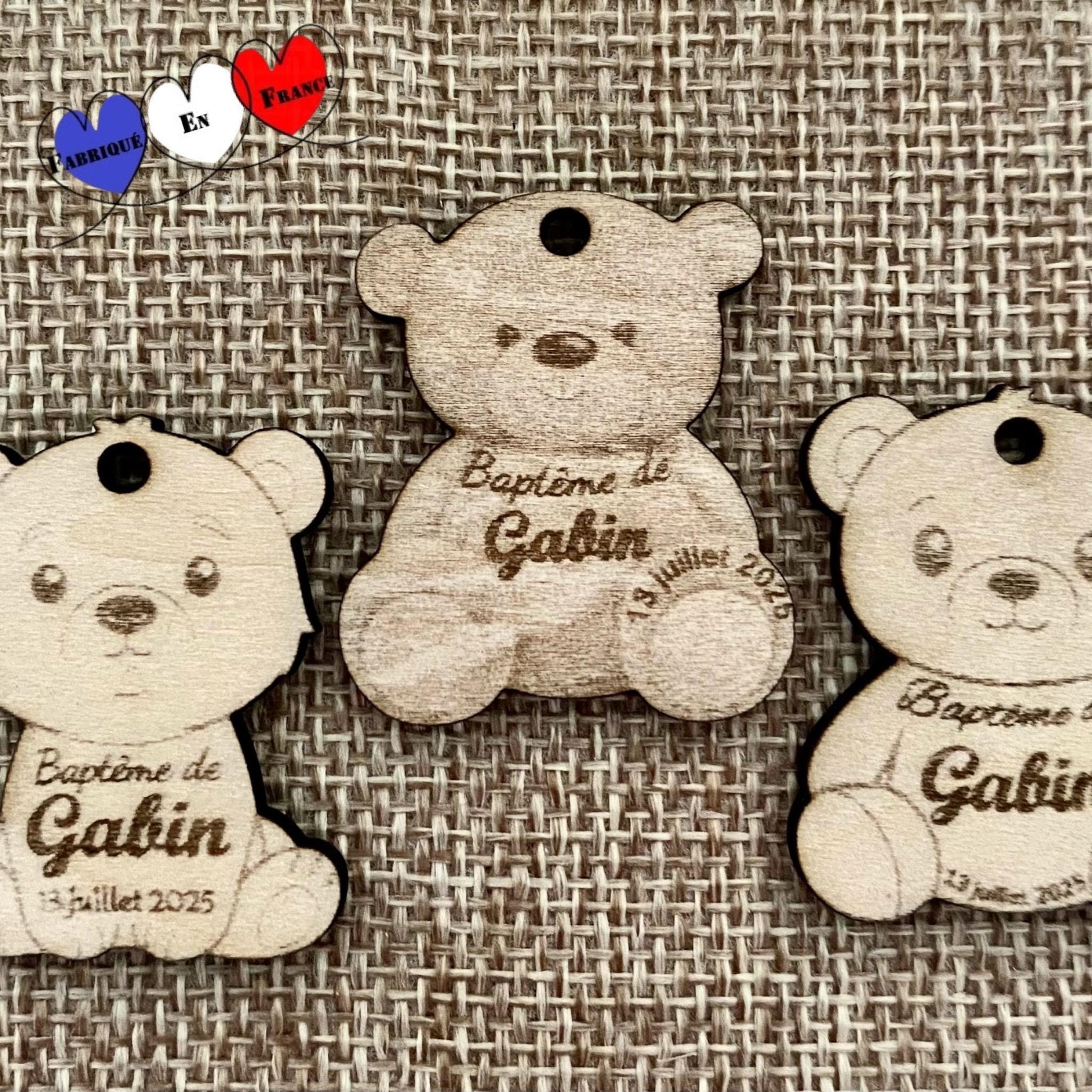 Étiquettes en bois en forme d'ourson avec gravure personnalisée 'Baptême de [Prénom]', posées sur un fond naturel."