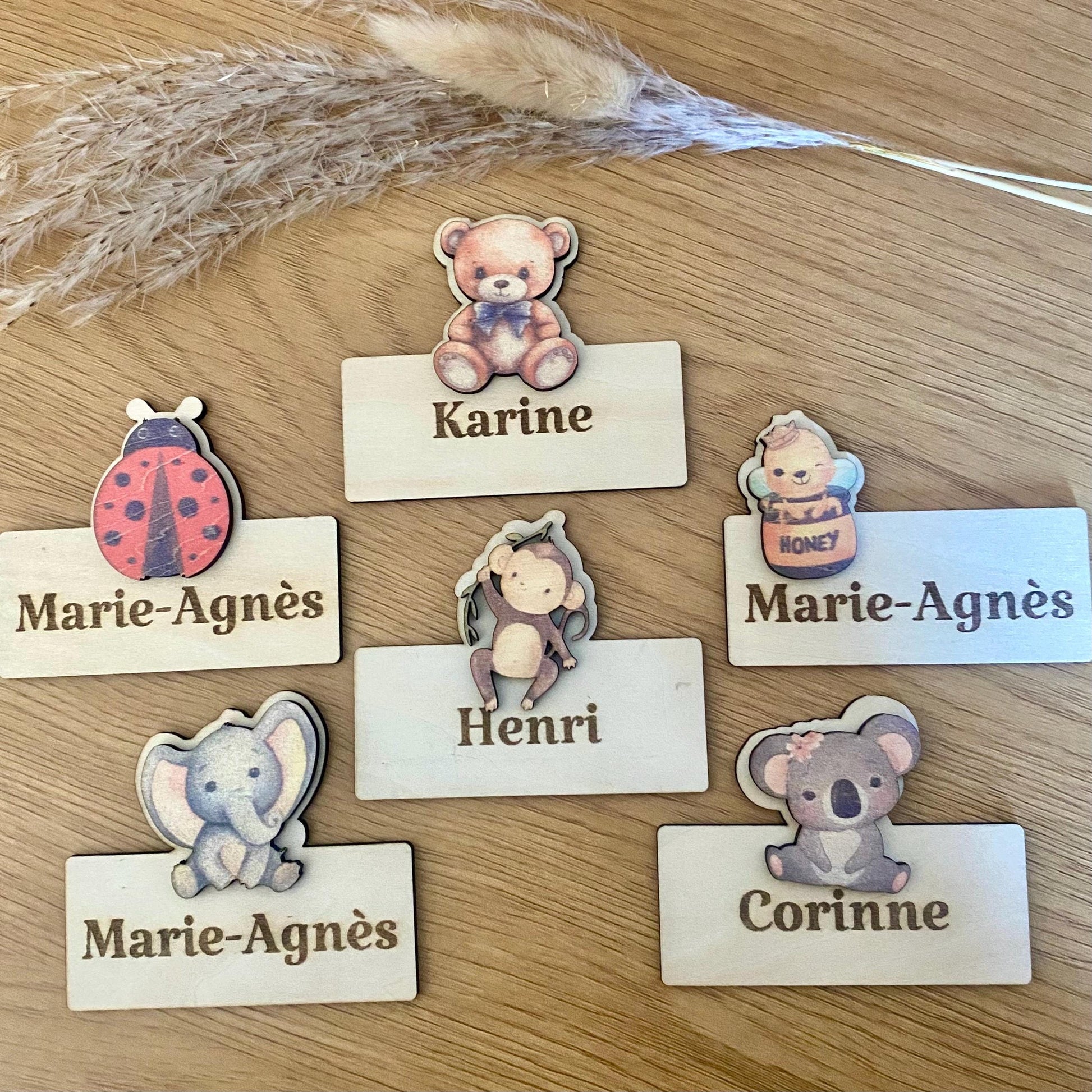 Lot de marque-places en bois personnalisés avec motifs animaux (koala, abeille, ourson) et prénoms gravés.