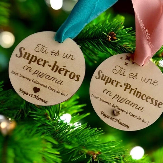 La suspension bois "Super-Héros" mise en valeur par un ruban coloré, et  La suspension bois "Super-Princesse" mise en valeur par un ruban coloré, avec une lumière douce et bienveillante.